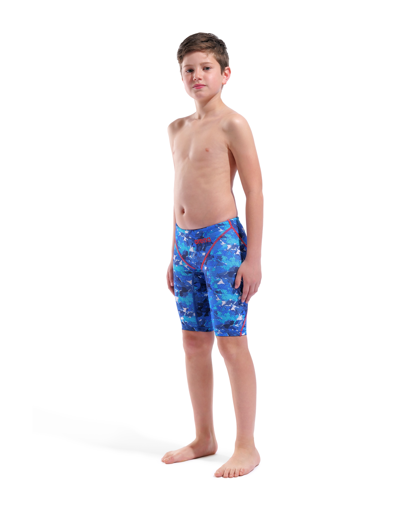 A boy stands barefoot against a white background, wearing Arena Boys Powerskin ST Next Jammer - Limited Edition - Splashy. The blue patterned racing jammers are World Aquatics approved and made from recycled fabric. He faces slightly to the side, neutral expression.