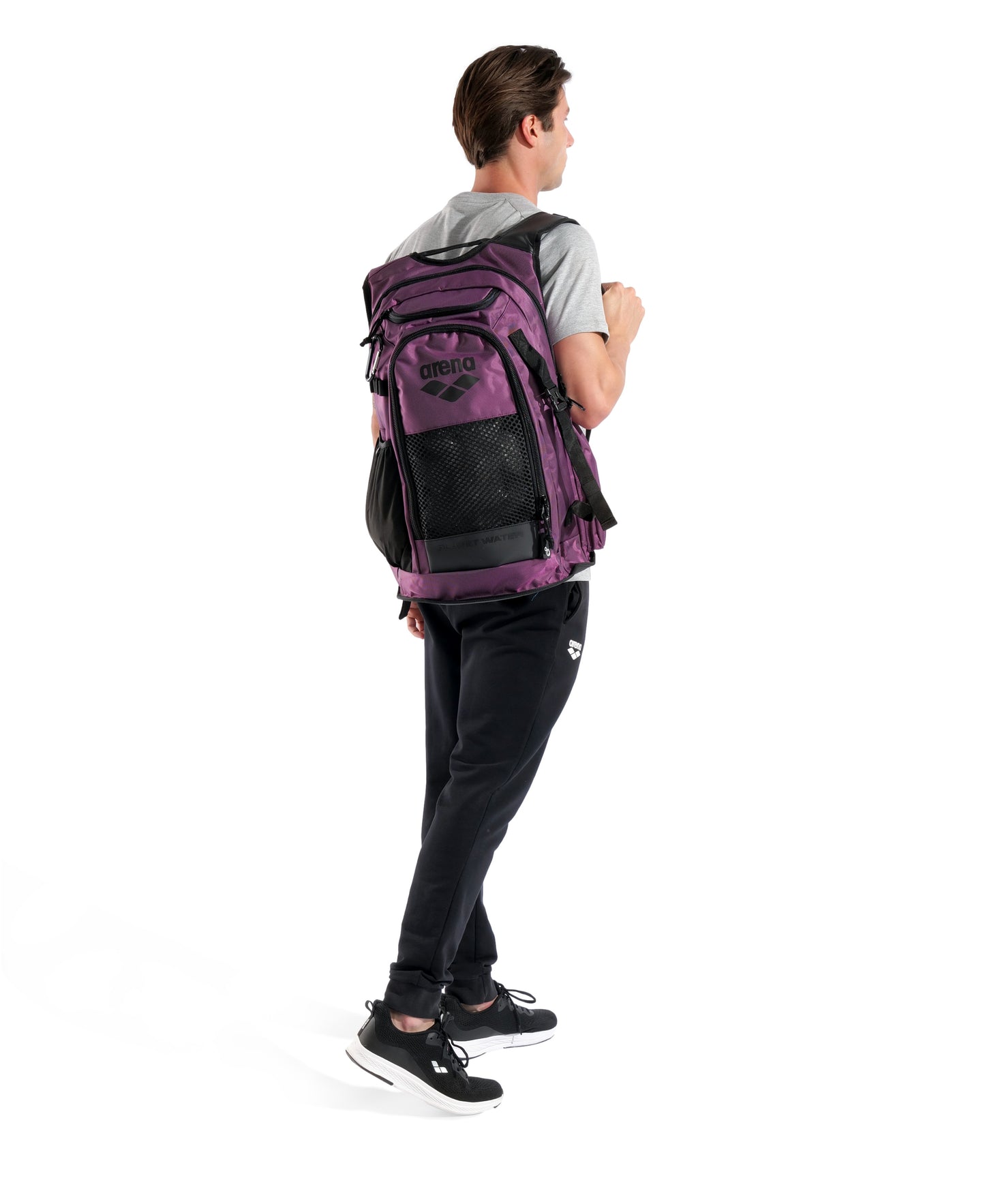 A person in a gray shirt and black pants stands facing away, carrying the Arena All Set Sports Swim Backpack 45L in Plum over one shoulder against a white background.