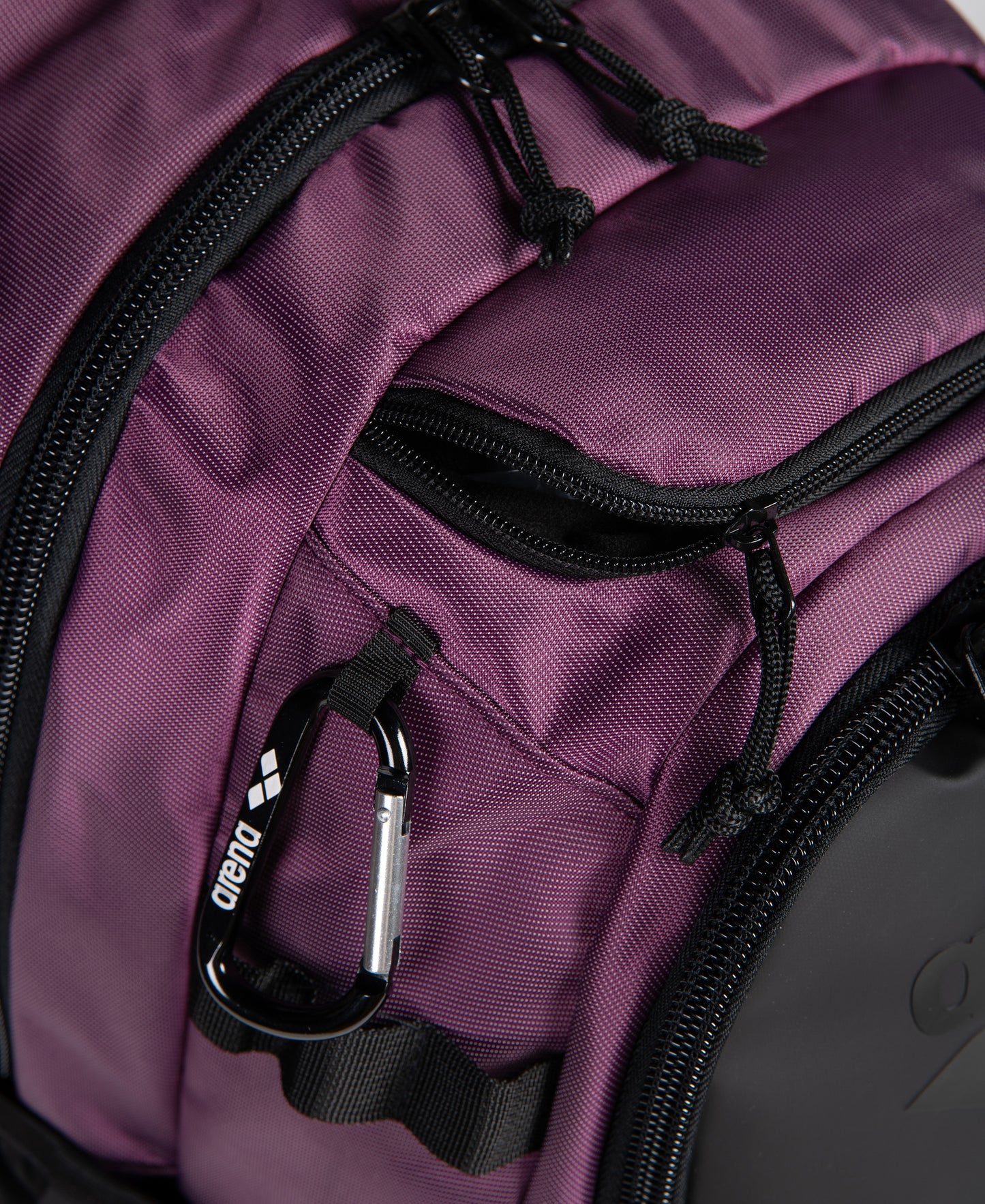 Close-up of the Arena All Set Sports Swim Backpack 45L in plum, featuring black zippers and a black-silver carabiner. Its textured fabric and partially open pockets showcase Arena’s practical wet management system.