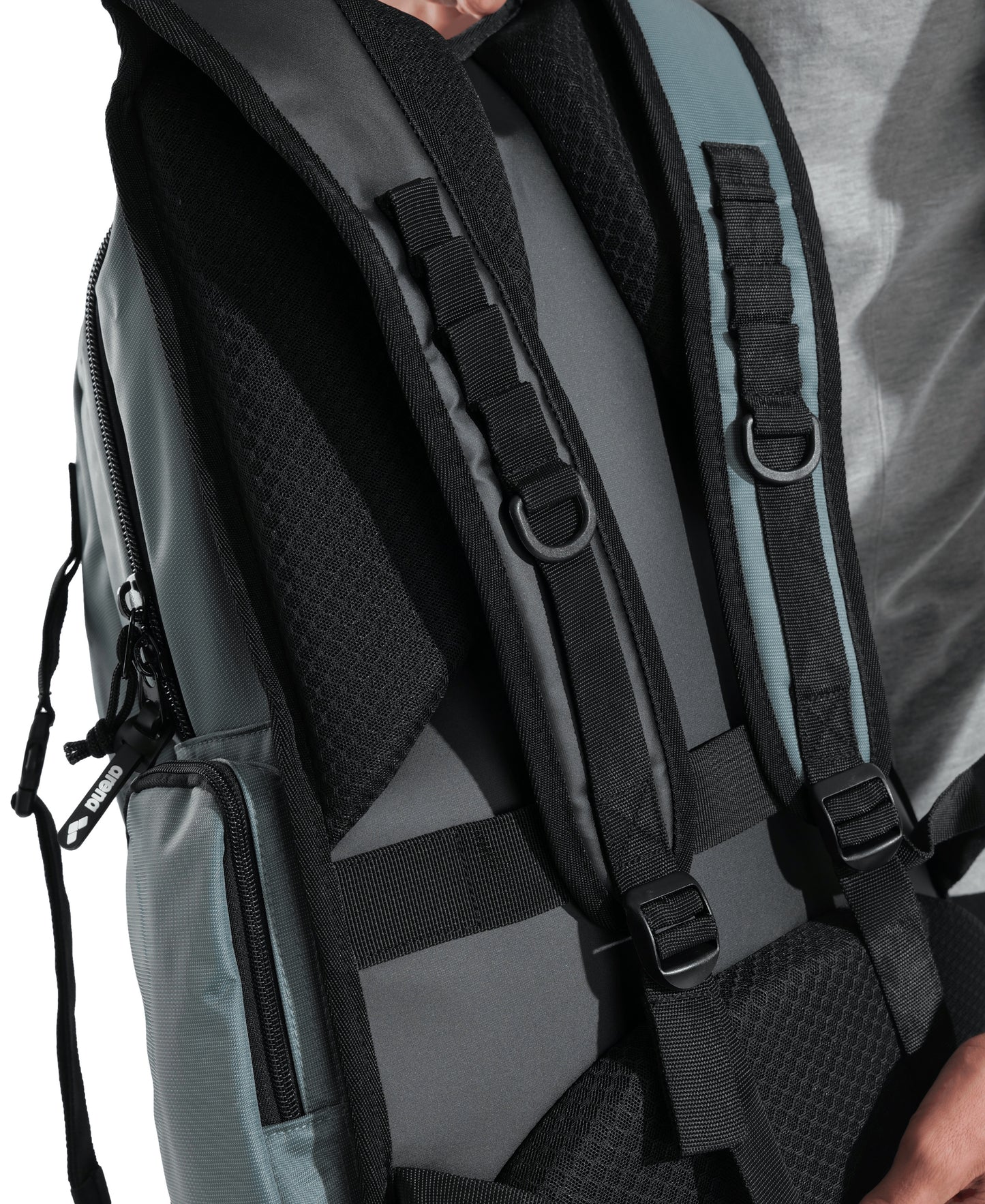 Close-up of someone in a light gray shirt wearing the Arena All Set Sports Swim Backpack 45L - Sage by Arena, featuring padded straps, adjustable buckles, a wet management system, and a side zipper pocket.